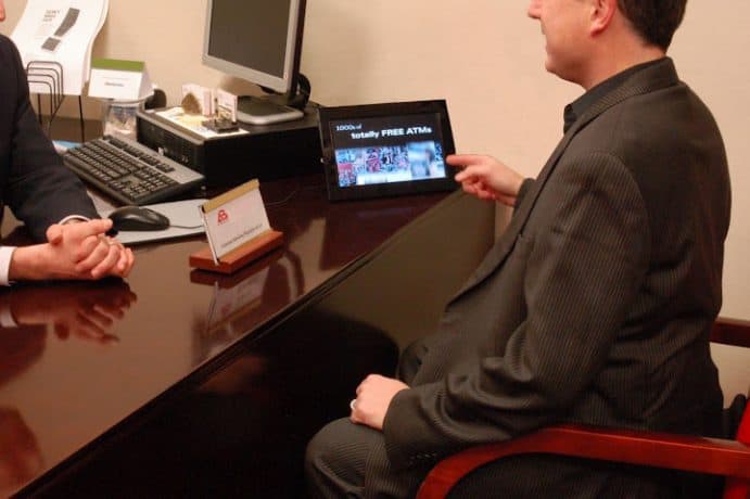 customer at bank desk pointing to mini digital sign